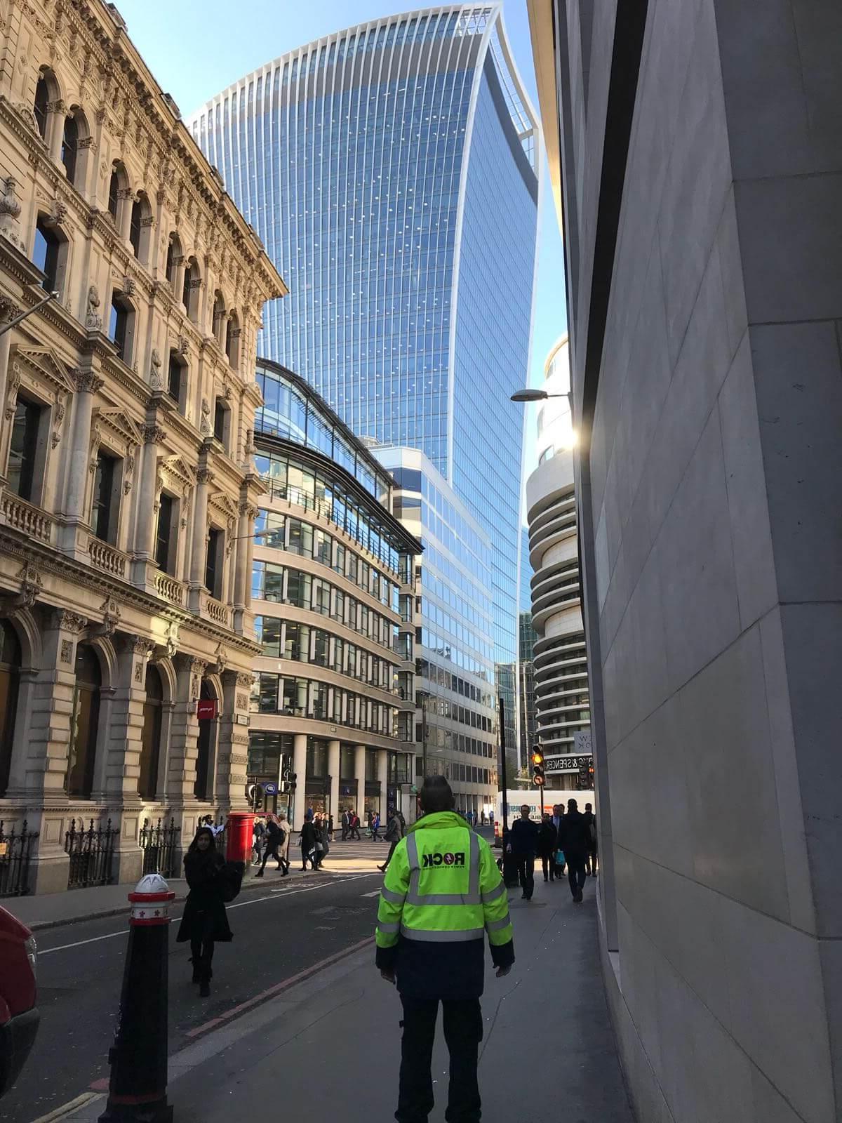 A 岩石电源连接 employee in a hi vis jacket, looking up at a London skyscraper building