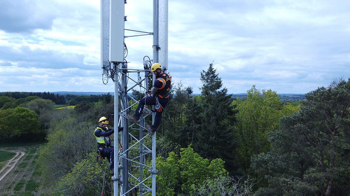 两名米铁员工站在电信塔顶，背景是绿树和田野